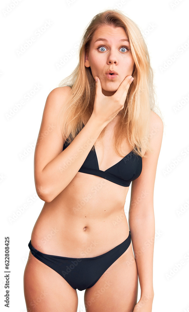Fototapeta premium Young beautiful blonde woman wearing bikini looking fascinated with disbelief, surprise and amazed expression with hands on chin