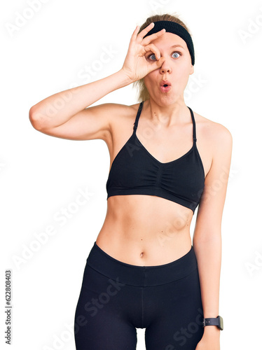 Young beautiful blonde woman wearing sportswear doing ok gesture shocked with surprised face, eye looking through fingers. unbelieving expression.