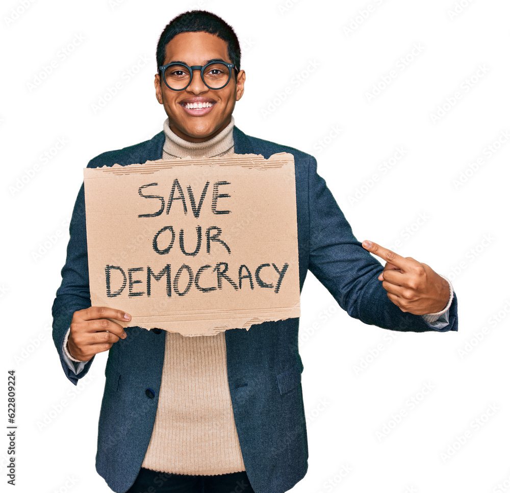 Young handsome hispanic man holding save our democracy protest banner smiling happy pointing with hand and finger Young handsome hispanic man holding save our democracy protest banner smiling happy pointing with hand and finger