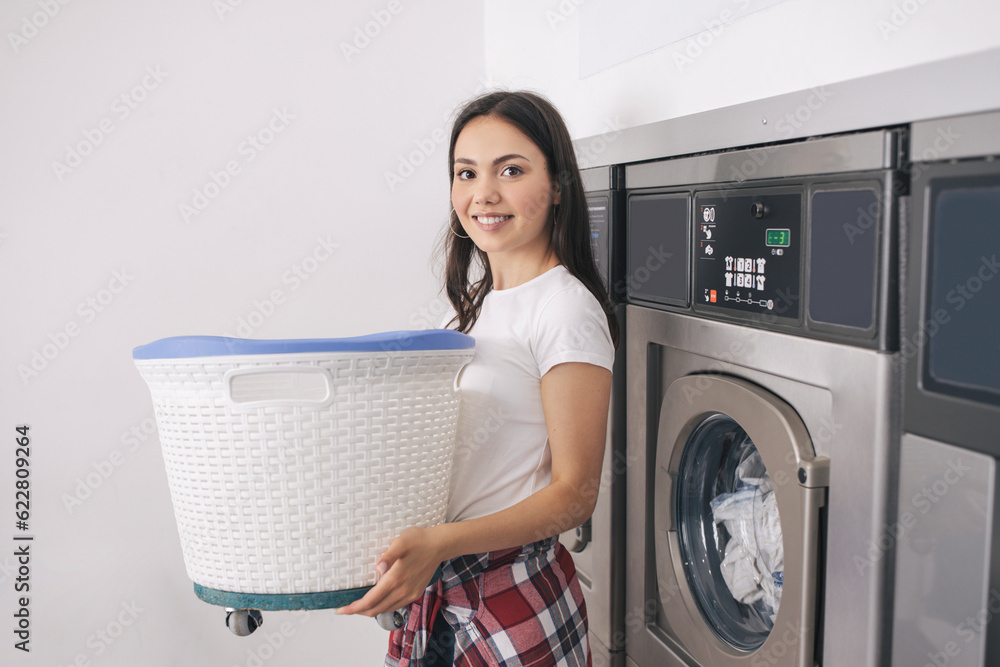 Happy Young Lady Doing Laundry At Laundrette, Posing Holding Basket Happy Young Lady Doing Laundry At Laundrette, Posing Holding Basket