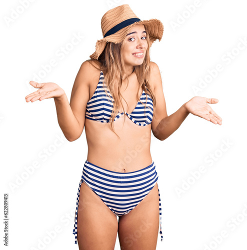 Young beautiful blonde woman wearing bikini and hat clueless and confused with open arms, no idea concept.