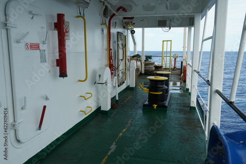 Entrance to white superstructure of container merchant vessel from  main deck painted green on port side. There are black bollard, red fire plan tube and mooring ropes in aft manoeuvring station.