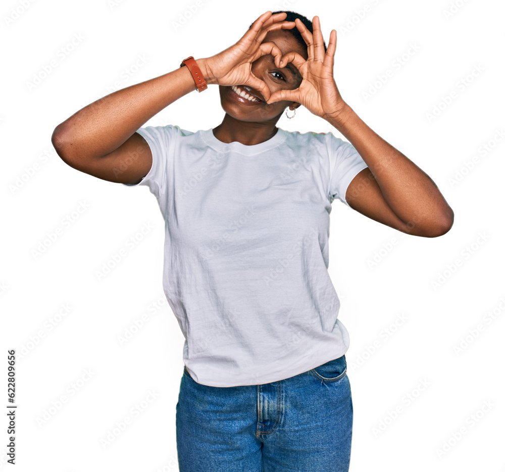 Young african american woman wearing casual white t shirt doing heart shape with hand and fingers smiling looking through sign