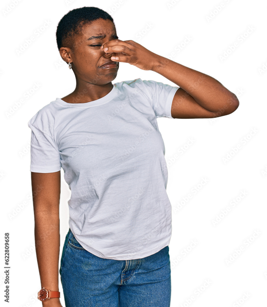 Young african american woman wearing casual white t shirt smelling something stinky and disgusting, intolerable smell, holding breath with fingers on nose. bad smell Young african american woman wearing casual white t shirt smelling something stinky and disgusting, intolerable smell, holding breath with fingers on nose. bad smell