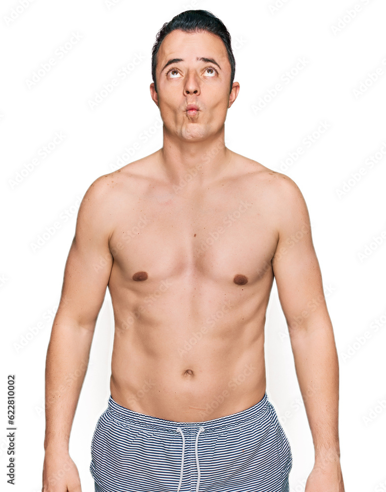 Fototapeta premium Handsome young man wearing swimwear shirtless making fish face with lips, crazy and comical gesture. funny expression.
