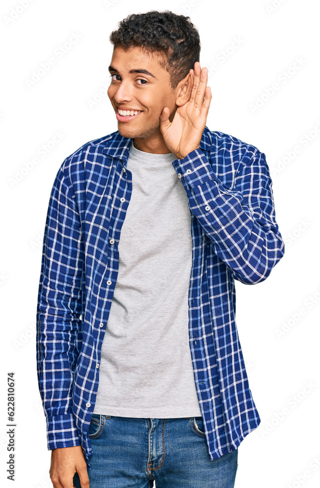 Young handsome african american man wearing casual clothes smiling with hand over ear listening an hearing to rumor or gossip. deafness concept. Young handsome african american man wearing casual clothes smiling with hand over ear listening an hearing to rumor or gossip. deafness concept.
