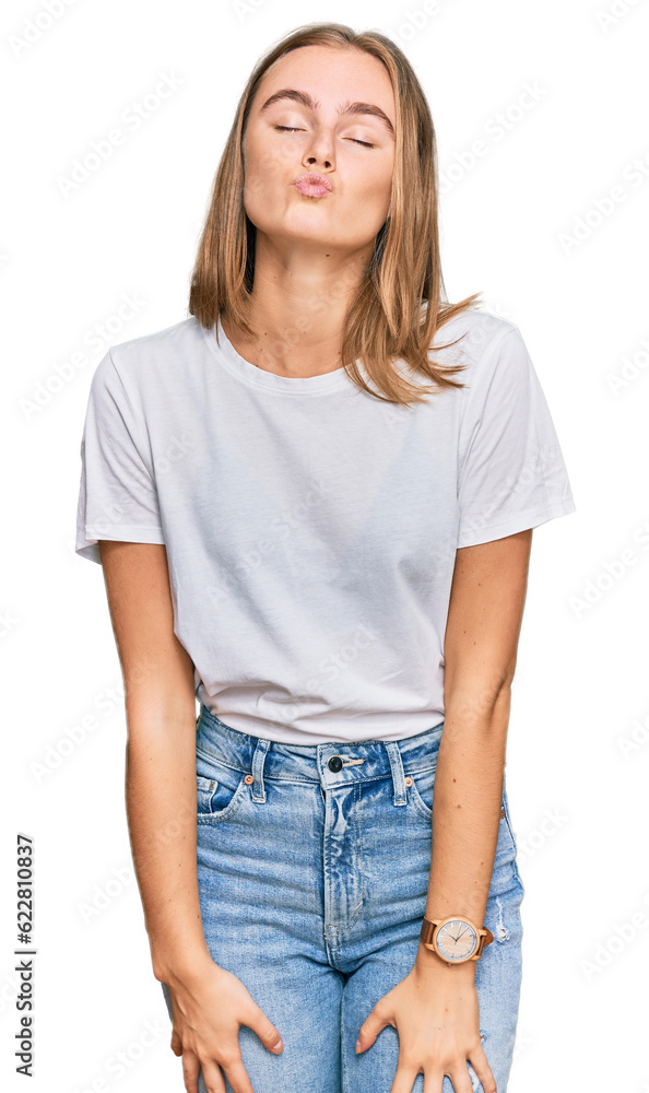 Beautiful young blonde woman wearing casual white t shirt looking at the camera blowing a kiss on air being lovely and sexy. love expression. Beautiful young blonde woman wearing casual white t shirt looking at the camera blowing a kiss on air being lovely and sexy. love expression.