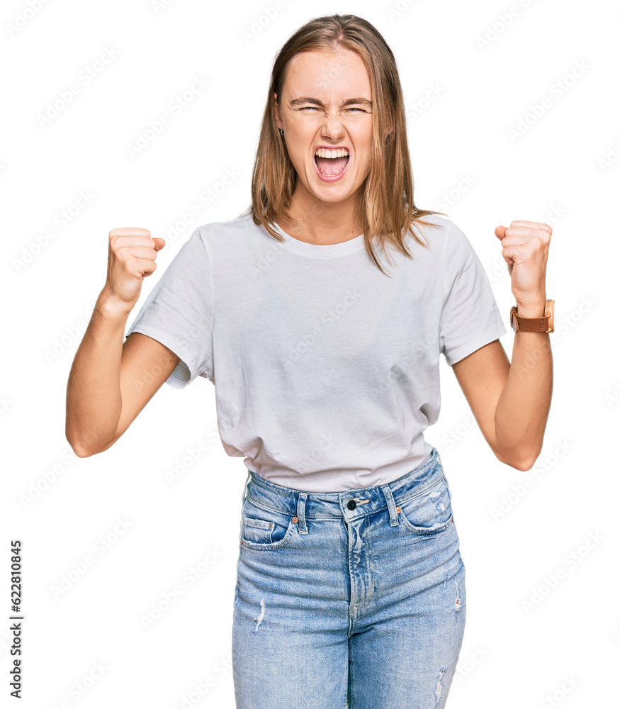 Beautiful young blonde woman wearing casual white t shirt angry and mad raising fists frustrated and furious while shouting with anger. rage and aggressive concept. Beautiful young blonde woman wearing casual white t shirt angry and mad raising fists frustrated and furious while shouting with anger. rage and aggressive concept.