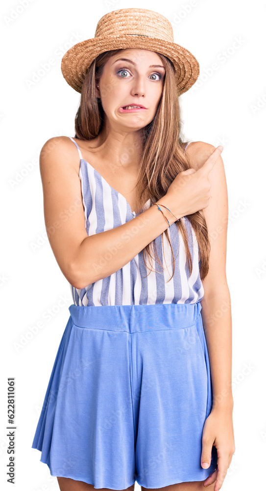 Young beautiful blonde woman wearing summer hat pointing aside worried and nervous with forefinger, concerned and surprised expression Young beautiful blonde woman wearing summer hat pointing aside worried and nervous with forefinger, concerned and surprised expression