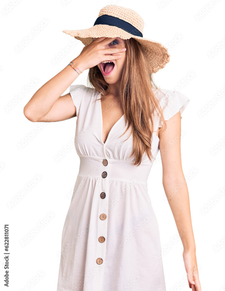 Young beautiful blonde woman wearing summer dress and hat peeking in shock covering face and eyes with hand, looking through fingers with embarrassed expression. Young beautiful blonde woman wearing summer dress and hat peeking in shock covering face and eyes with hand, looking through fingers with embarrassed expression.