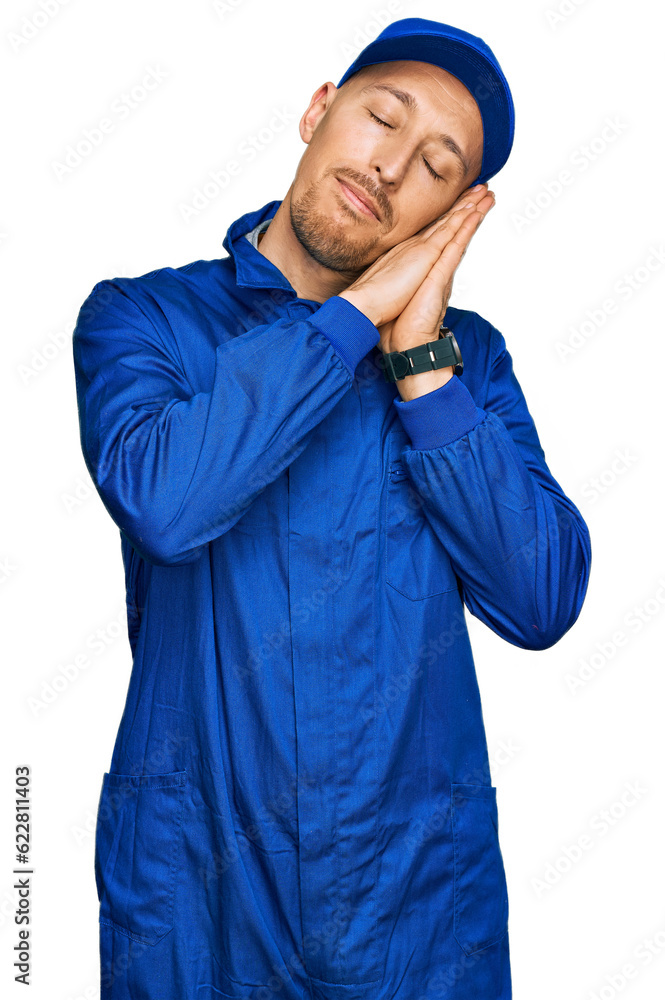 Bald man with beard wearing builder jumpsuit uniform sleeping tired dreaming and posing with hands together while smiling with closed eyes. Bald man with beard wearing builder jumpsuit uniform sleeping tired dreaming and posing with hands together while smiling with closed eyes.