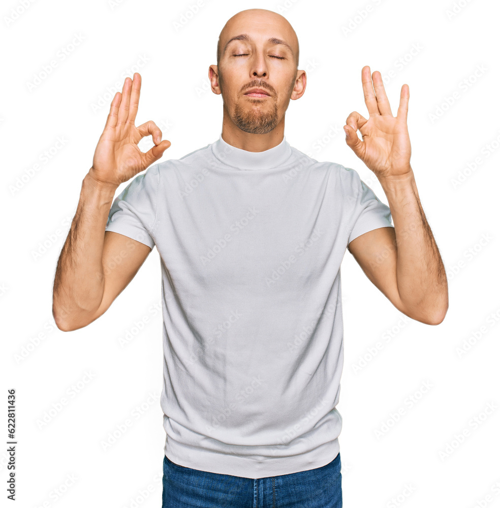 Bald man with beard wearing casual white t shirt relax and smiling with eyes closed doing meditation gesture with fingers. yoga concept. Bald man with beard wearing casual white t shirt relax and smiling with eyes closed doing meditation gesture with fingers. yoga concept.