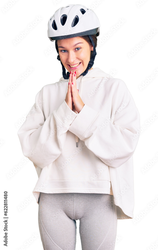 Beautiful brunette young woman wearing bike helmet and sporty clothes praying with hands together asking for forgiveness smiling confident. Beautiful brunette young woman wearing bike helmet and sporty clothes praying with hands together asking for forgiveness smiling confident.