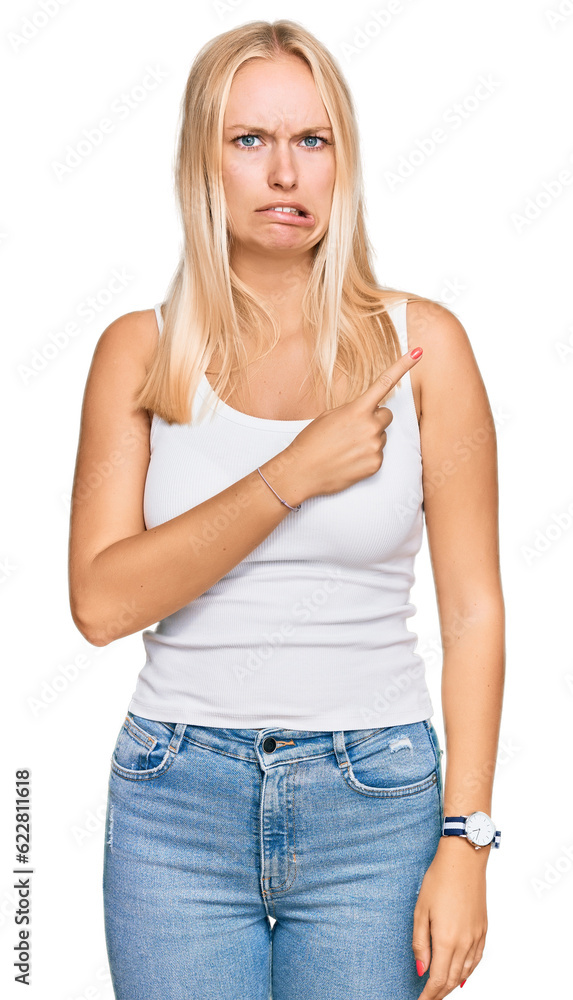 Young blonde girl wearing casual style with sleeveless shirt pointing aside worried and nervous with forefinger, concerned and surprised expression Young blonde girl wearing casual style with sleeveless shirt pointing aside worried and nervous with forefinger, concerned and surprised expression