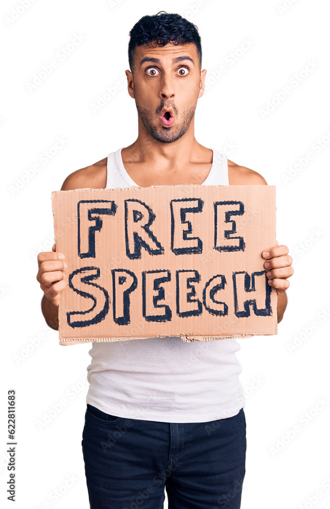 Young hispanic man holding free speech banner scared and amazed with open mouth for surprise, disbelief face Young hispanic man holding free speech banner scared and amazed with open mouth for surprise, disbelief face