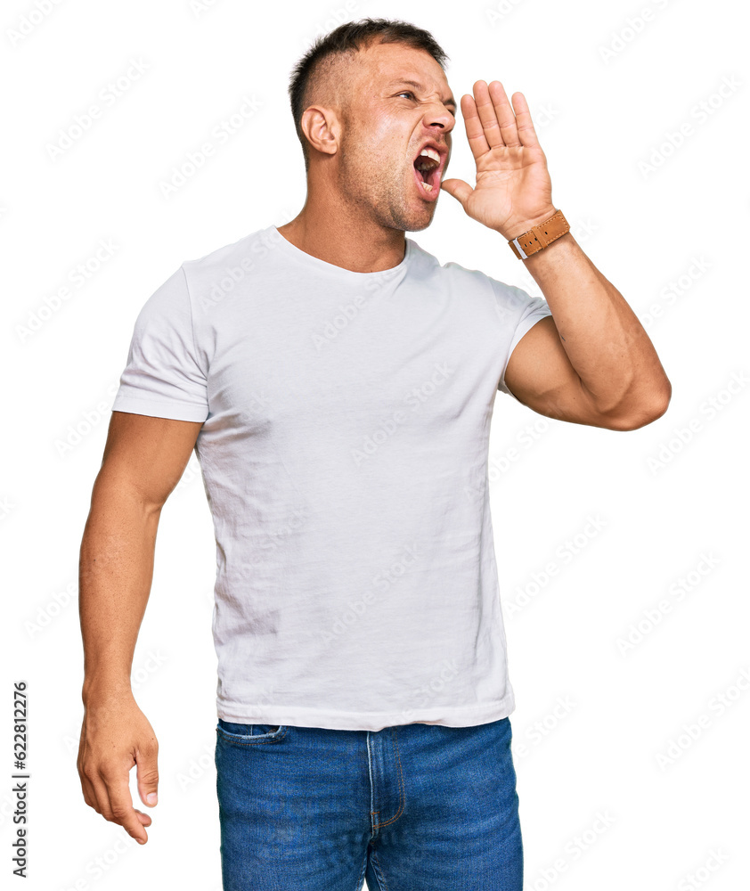 Handsome muscle man wearing casual white tshirt shouting and screaming loud to side with hand on mouth. communication concept. Handsome muscle man wearing casual white tshirt shouting and screaming loud to side with hand on mouth. communication concept.