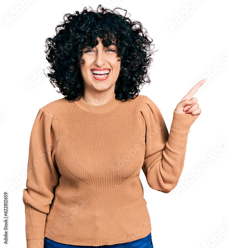 Young middle east girl pointing with finger to the side smiling and laughing hard out loud because funny crazy joke.