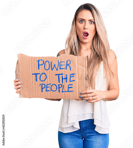 Young beautiful blonde woman holding power to the people cardboard banner scared and amazed with open mouth for surprise, disbelief face