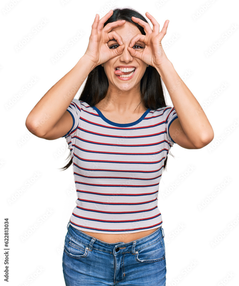 Young hispanic girl wearing casual striped t shirt doing ok gesture like binoculars sticking tongue out, eyes looking through fingers. crazy expression. Young hispanic girl wearing casual striped t shirt doing ok gesture like binoculars sticking tongue out, eyes looking through fingers. crazy expression.