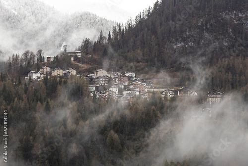 View of Cibiana di Cadore, small town in the mountains in a misty winter day  Snow peaked mountains on the background  Belluno, Italy  Dolomites © cabuscaa