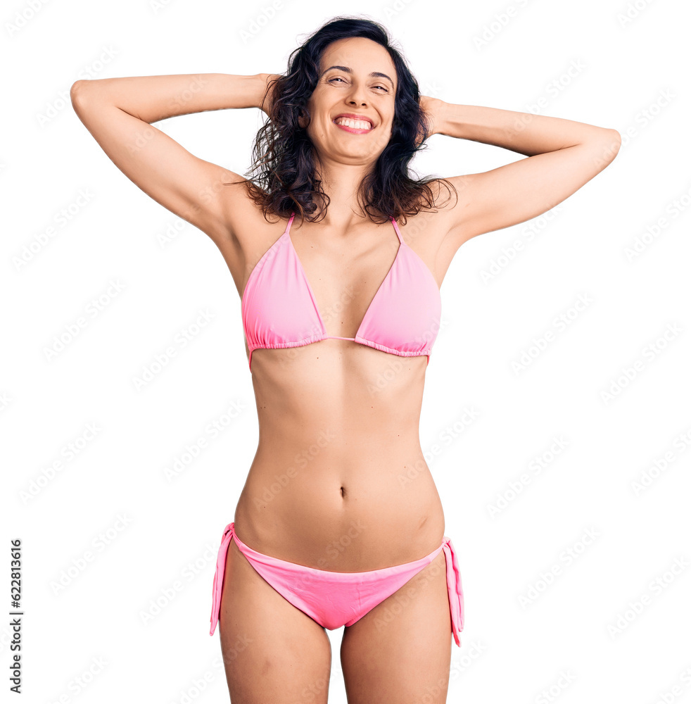 Obraz premium Young beautiful hispanic woman wearing bikini relaxing and stretching, arms and hands behind head and neck smiling happy