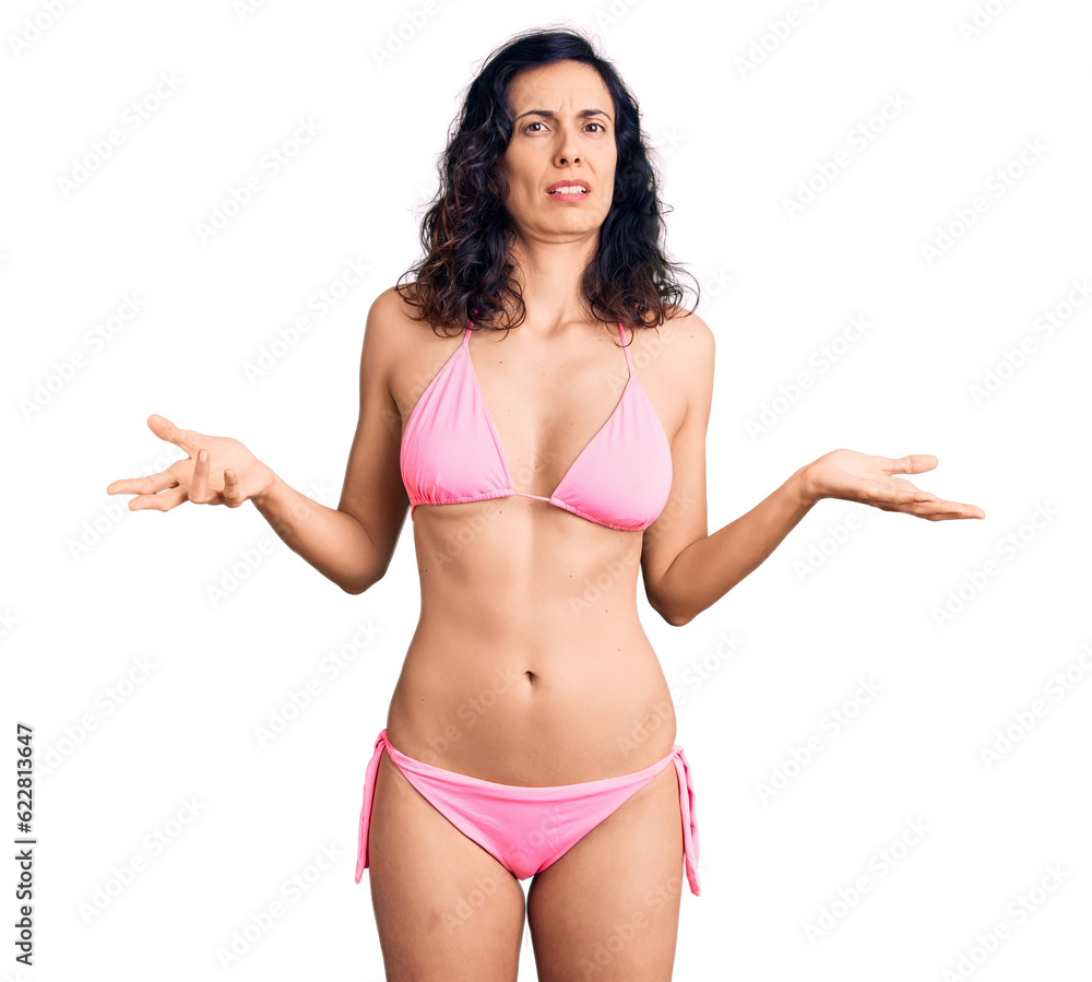 Fototapeta premium Young beautiful hispanic woman wearing bikini clueless and confused with open arms, no idea concept.