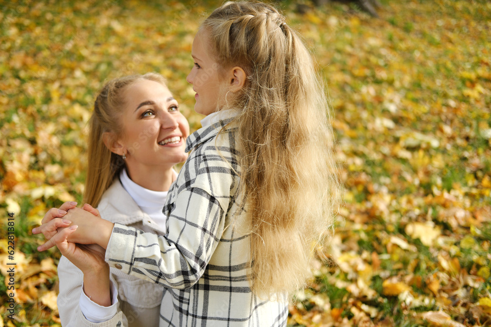 Fototapeta premium Mother and daughter spend time together in the autumn park. Mother looks at her daughter and smiles