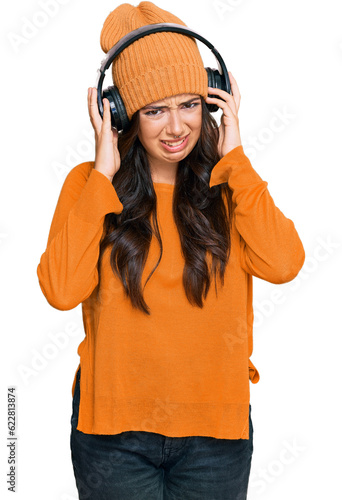 Beautiful brunette young woman listening to music using headphones covering ears with fingers with annoyed expression for the noise of loud music. deaf concept.