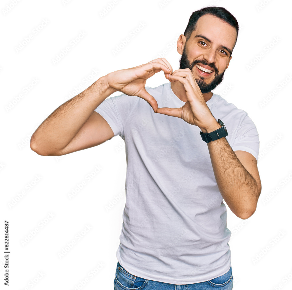 Young man with beard wearing casual white t shirt smiling in love doing heart symbol shape with hands. romantic concept. Young man with beard wearing casual white t shirt smiling in love doing heart symbol shape with hands. romantic concept.