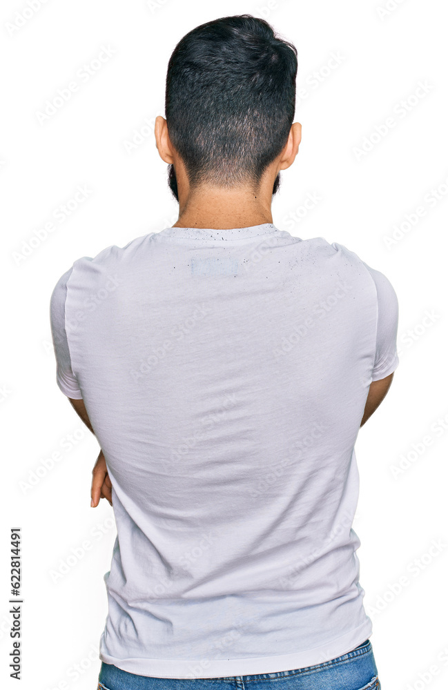 Young man with beard wearing casual white t shirt standing backwards looking away with crossed arms Young man with beard wearing casual white t shirt standing backwards looking away with crossed arms