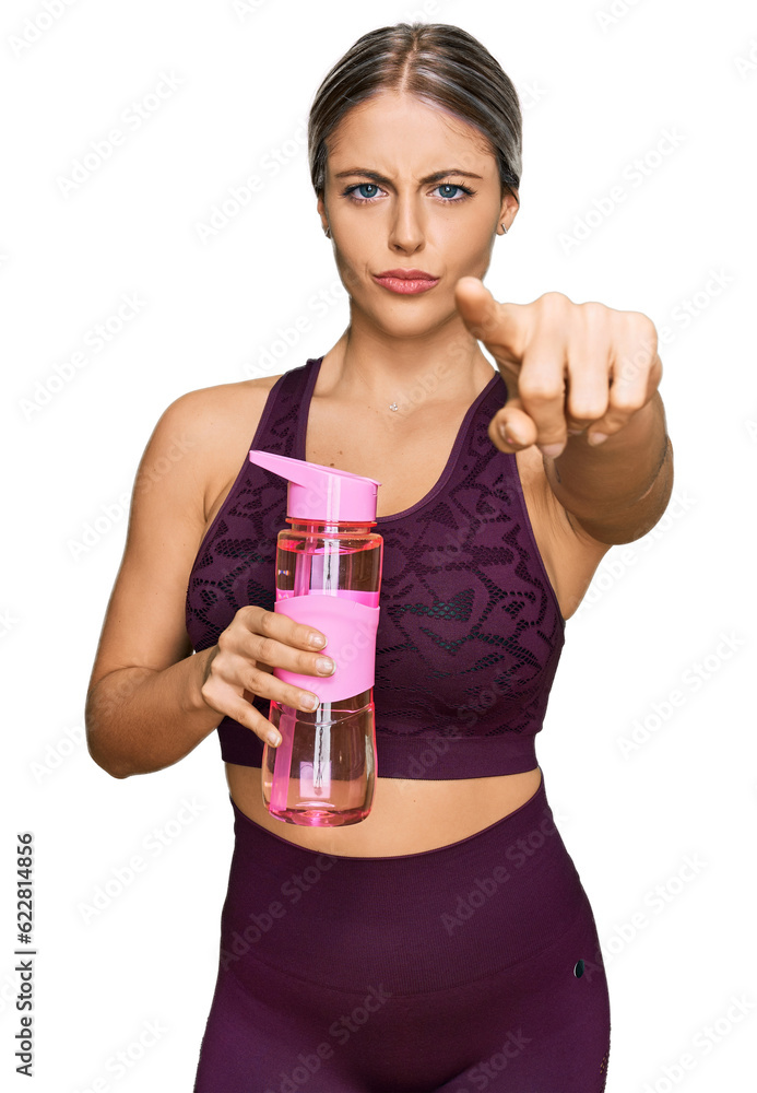 Beautiful blonde woman wearing sportswear holding water bottle pointing with finger to the camera and to you, confident gesture looking serious Beautiful blonde woman wearing sportswear holding water bottle pointing with finger to the camera and to you, confident gesture looking serious