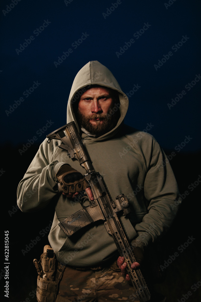 Portrait of a bearded Ukrainian warrior in hoody with his rifle looking in the camera Portrait of a bearded Ukrainian warrior in hoody with his rifle looking in the camera
