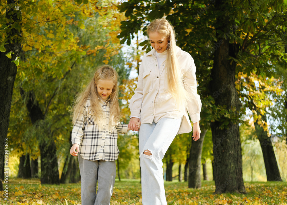 Family spend time together in autumn park. Mother and daughter are walking in the autumn park and throwing leaves up with their feet