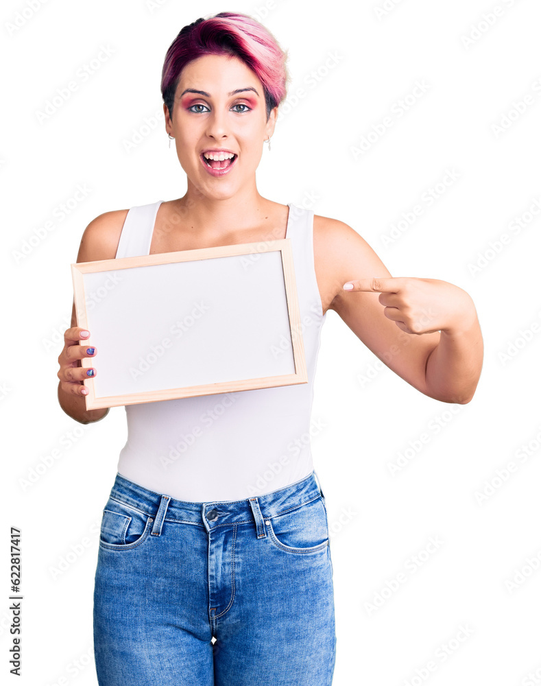 Young beautiful woman with pink hair holding empty white chalkboard smiling happy pointing with hand and finger Young beautiful woman with pink hair holding empty white chalkboard smiling happy pointing with hand and finger