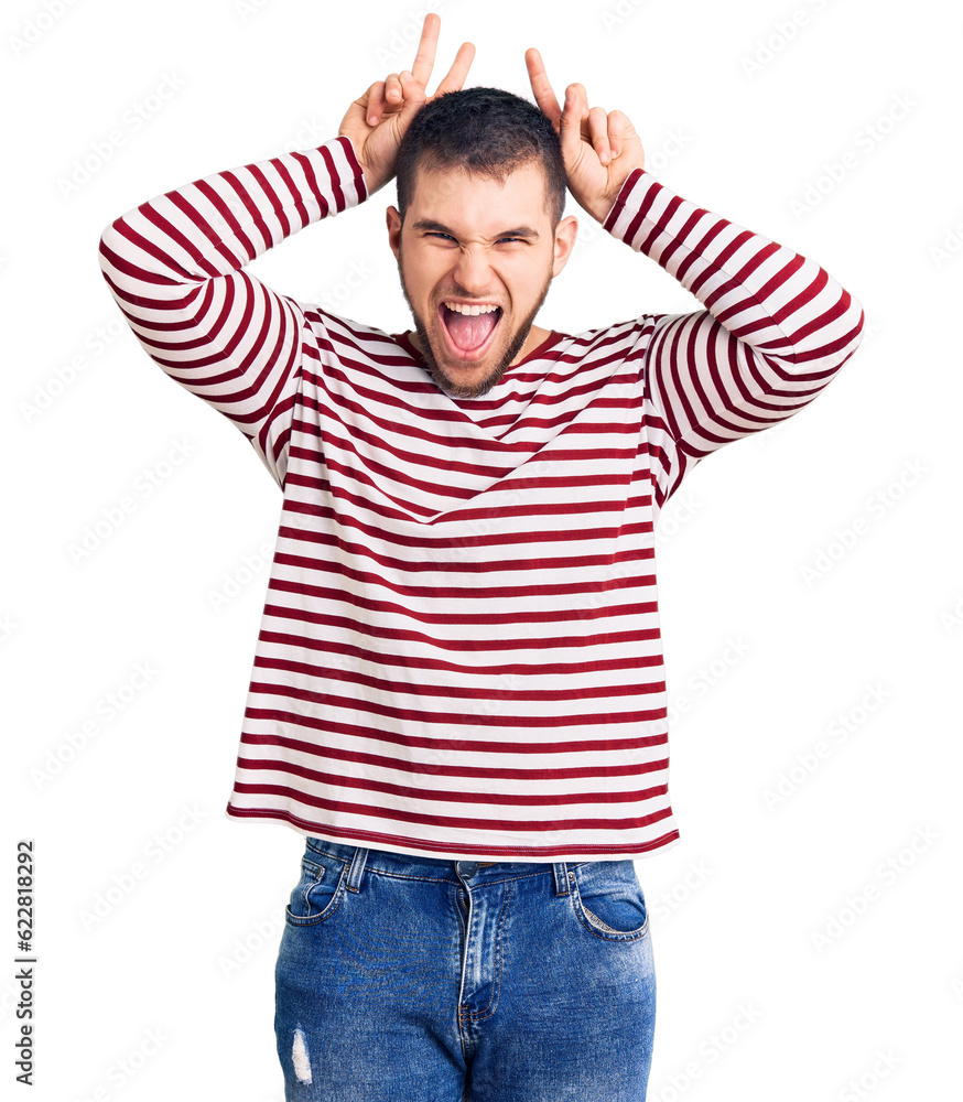 Fototapeta premium Young handsome man wearing striped sweater posing funny and crazy with fingers on head as bunny ears, smiling cheerful