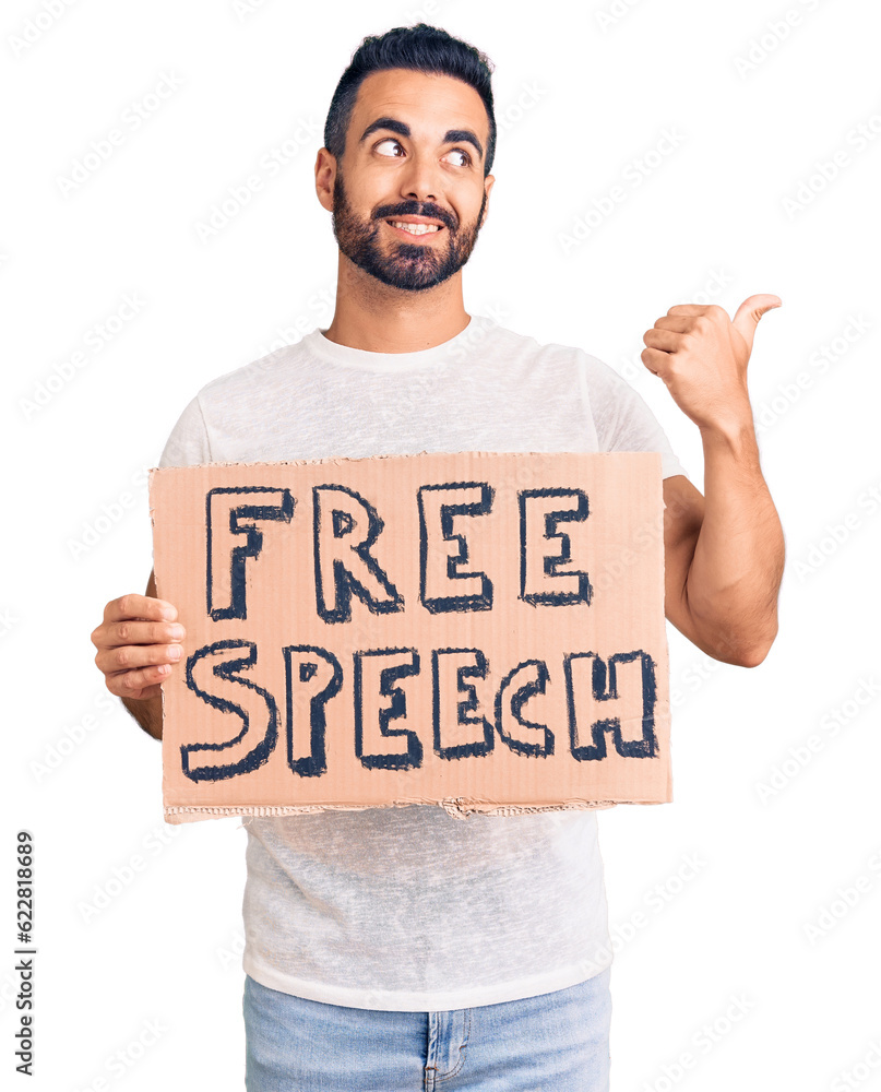 Young hispanic man holding free speech banner pointing thumb up to the side smiling happy with open mouth Young hispanic man holding free speech banner pointing thumb up to the side smiling happy with open mouth