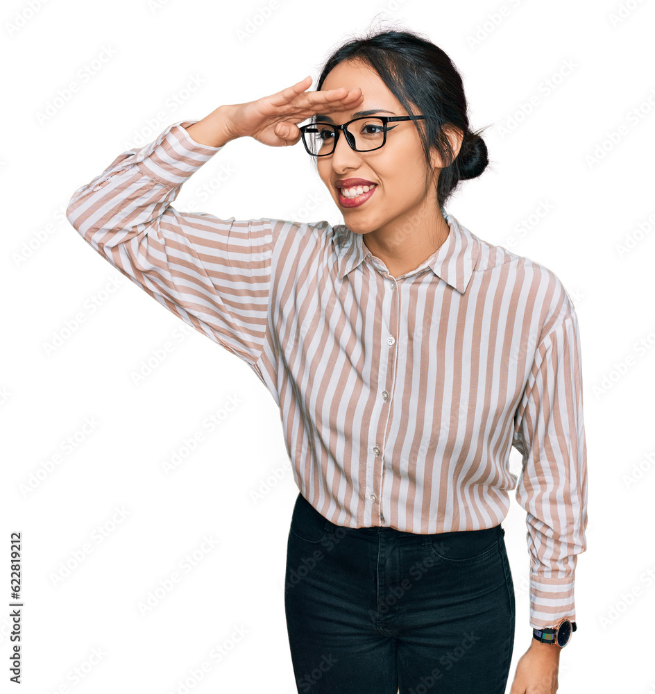 Young hispanic girl wearing casual clothes and glasses very happy and smiling looking far away with hand over head. searching concept.