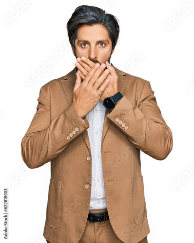 Young hispanic man wearing business clothes shocked covering mouth with hands for mistake. secret concept.