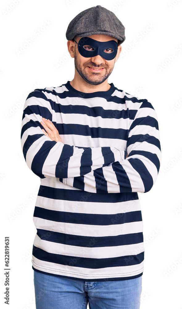 Young handsome man wearing burglar mask happy face smiling with crossed arms looking at the camera. positive person. Young handsome man wearing burglar mask happy face smiling with crossed arms looking at the camera. positive person.