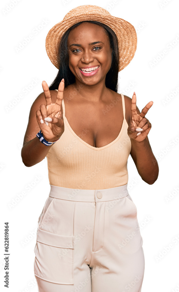 Young black woman wearing summer hat smiling looking to the camera showing fingers doing victory sign. number two. Young black woman wearing summer hat smiling looking to the camera showing fingers doing victory sign. number two.