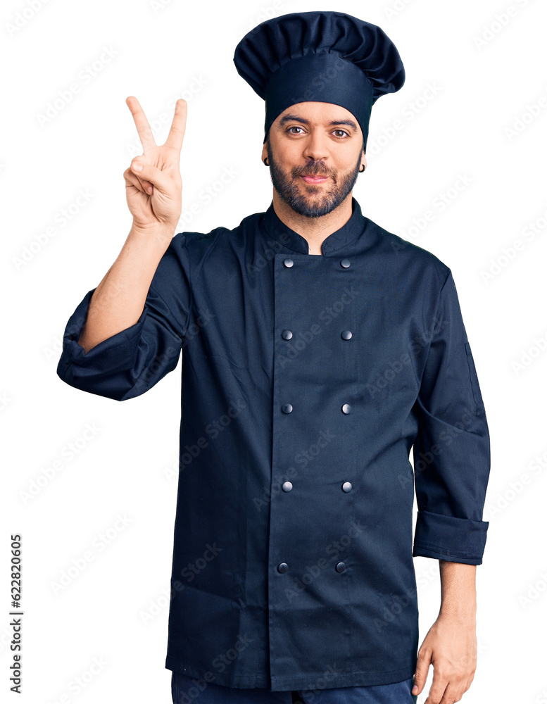 Young hispanic man wearing cooker uniform showing and pointing up with fingers number two while smiling confident and happy. Young hispanic man wearing cooker uniform showing and pointing up with fingers number two while smiling confident and happy.