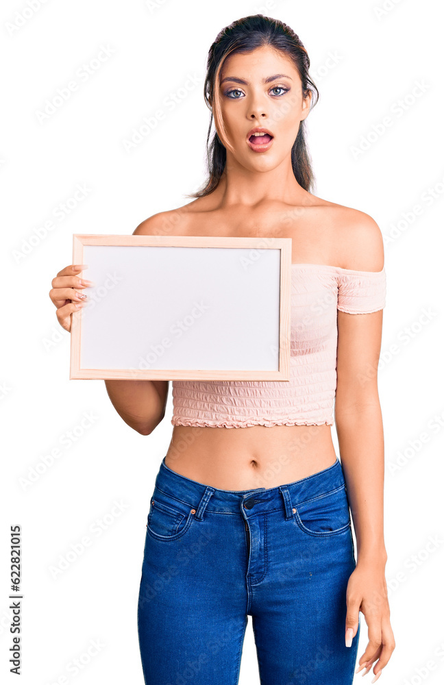 Young beautiful woman holding empty white chalkboard scared and amazed with open mouth for surprise, disbelief face Young beautiful woman holding empty white chalkboard scared and amazed with open mouth for surprise, disbelief face