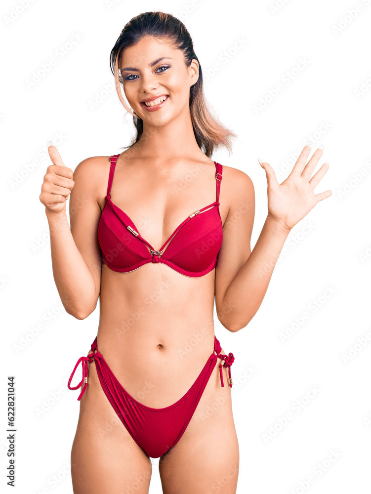 Young beautiful woman wearing bikini showing and pointing up with fingers number six while smiling confident and happy. Young beautiful woman wearing bikini showing and pointing up with fingers number six while smiling confident and happy.