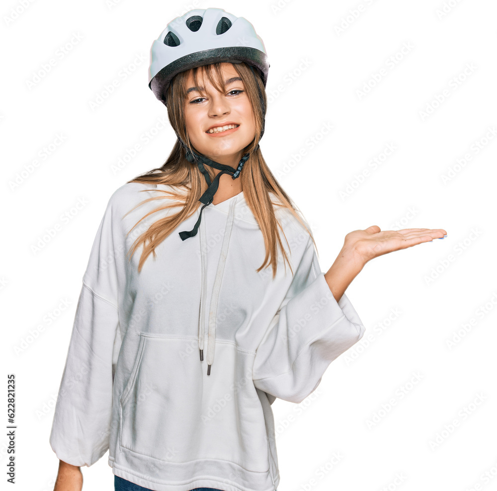 Teenager caucasian girl wearing bike helmet smiling cheerful presenting and pointing with palm of hand looking at the camera. Teenager caucasian girl wearing bike helmet smiling cheerful presenting and pointing with palm of hand looking at the camera.