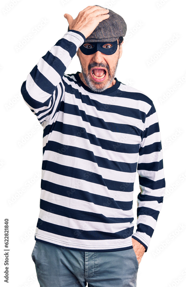 Middle age handsome man wearing burglar mask surprised with hand on head for mistake, remember error. forgot, bad memory concept. Middle age handsome man wearing burglar mask surprised with hand on head for mistake, remember error. forgot, bad memory concept.