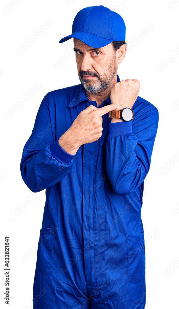 Middle age handsome man wearing mechanic uniform in hurry pointing to watch time, impatience, looking at the camera with relaxed expression Middle age handsome man wearing mechanic uniform in hurry pointing to watch time, impatience, looking at the camera with relaxed expression