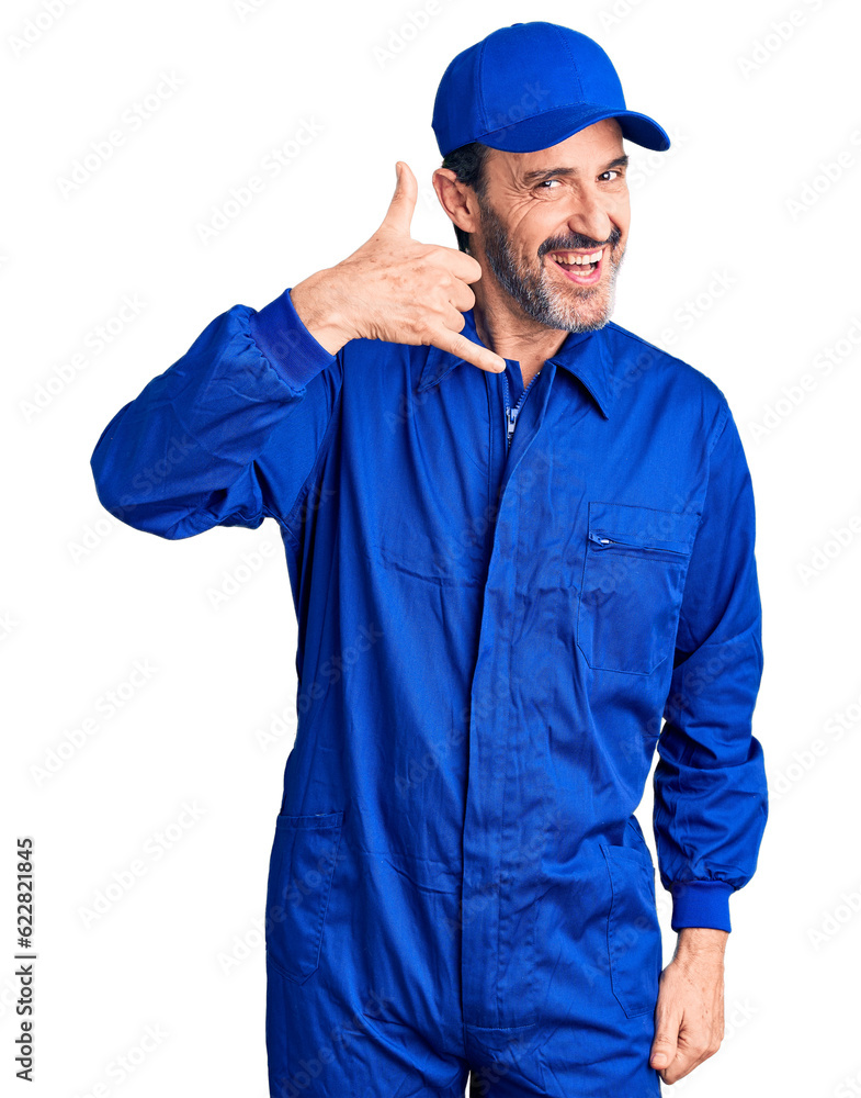 Middle age handsome man wearing mechanic uniform smiling doing phone gesture with hand and fingers like talking on the telephone. communicating concepts.