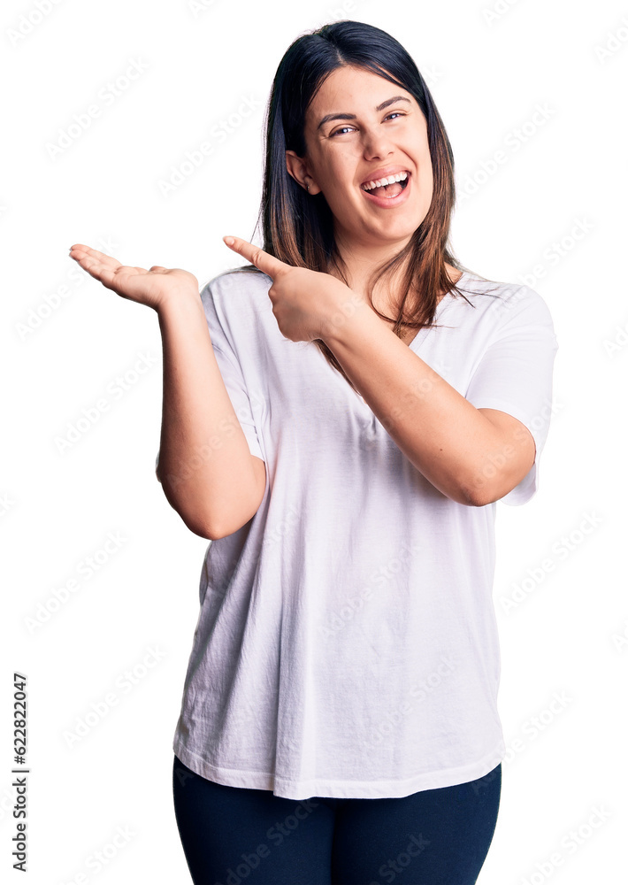 Young beautiful brunette woman wearing casual t-shirt amazed and smiling to the camera while presenting with hand and pointing with finger. Young beautiful brunette woman wearing casual t-shirt amazed and smiling to the camera while presenting with hand and pointing with finger.