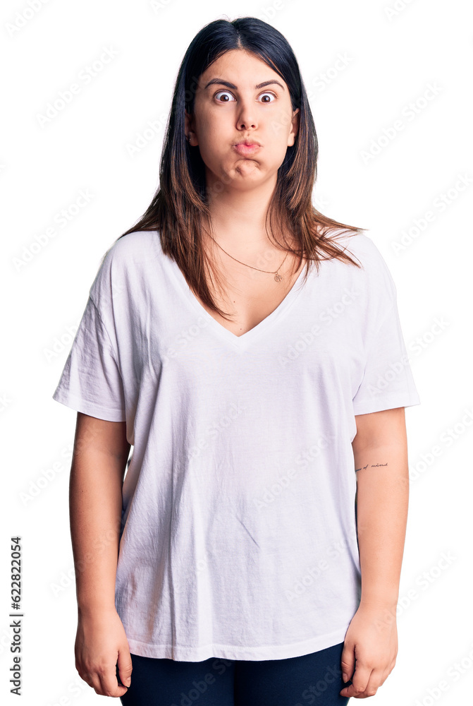 Young beautiful brunette woman wearing casual t-shirt puffing cheeks with funny face. mouth inflated with air, crazy expression. Young beautiful brunette woman wearing casual t-shirt puffing cheeks with funny face. mouth inflated with air, crazy expression.