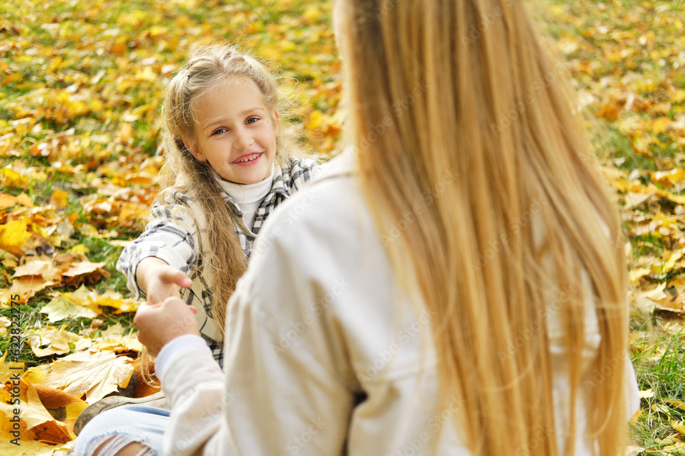 The family has fun in the park. The girl and mother sit on a blanket and rest. Daughter looks at the camera and smiles